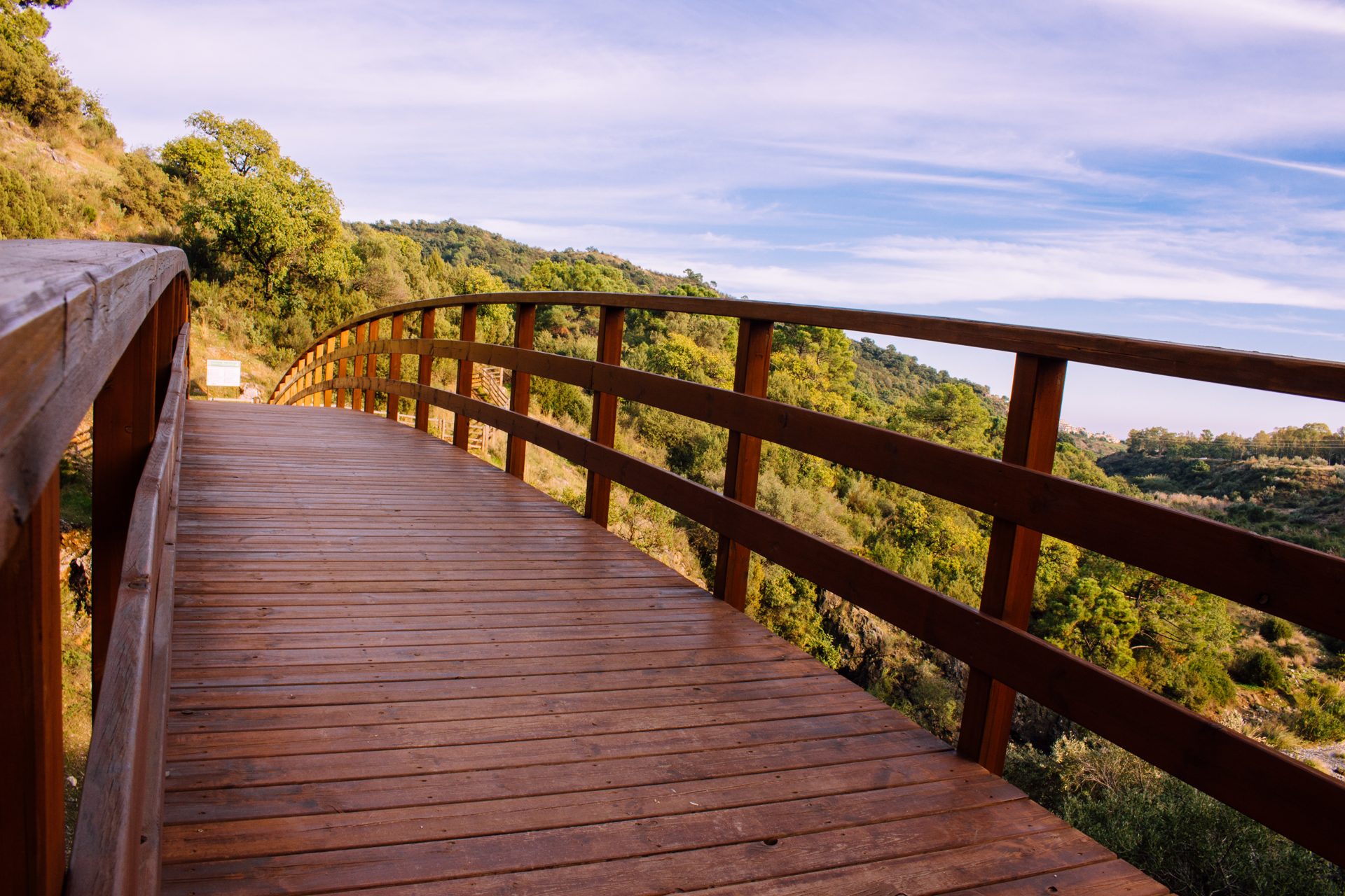 Wooden walkway with scenic view of lush green hills and clear blue sky.